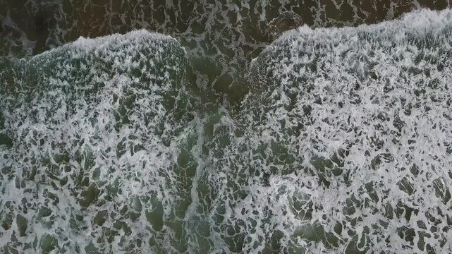 Aerial view of the crashing waves at Legzira Beach, showing white sea foam and dark ocean water in Tiznit, MOROCCO.