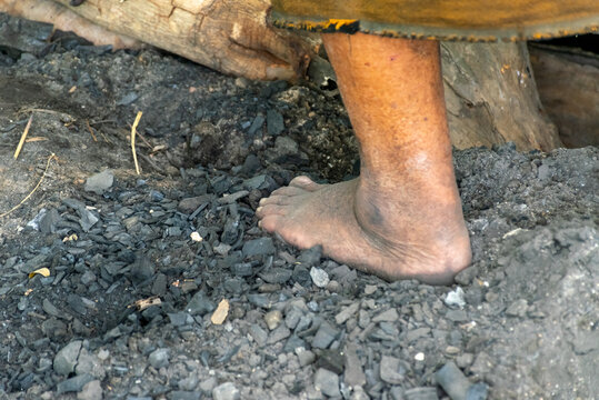 Close view of barefoot worker standing charcoal ash near wooden logs showing traditional manual labor rustic outdoor working environment