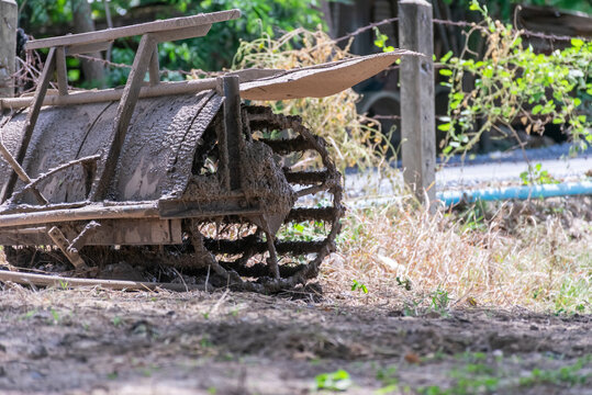 Mud covered walking tiller metal cage wheel resting beside rural rice field after soil preparation agricultural work