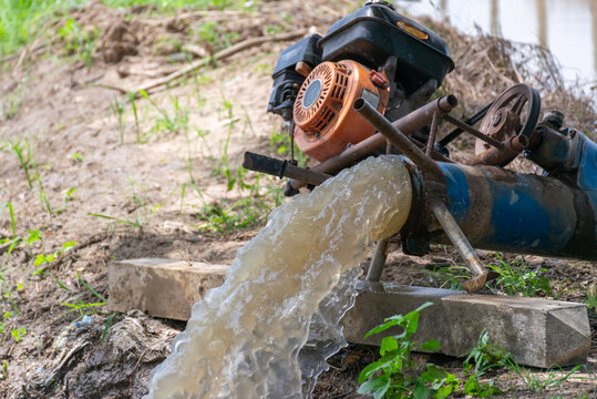 Engine powered water pump discharges strong stream of water for irrigation drainage rural farmland showing agricultural water management