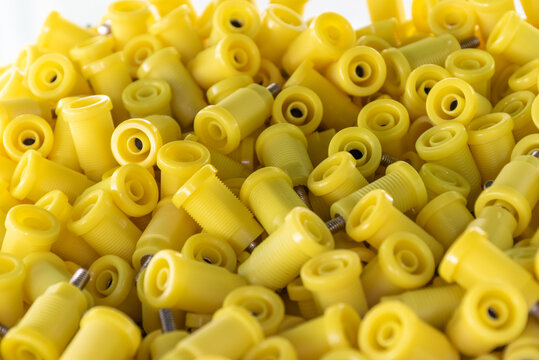 Close up of numerous yellow plastic threaded components metal inserts arranged pile showing industrial manufacturing parts hardware production