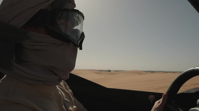 Driver wrapped in a scarf and dust goggles steering a buggy across desert sand Morocco