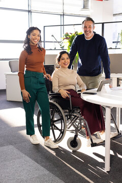 Diverse coworkers collaborating around white table in open office with manual wheelchair and tablet