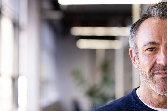 Mature professional standing in blurred office corridor with floor-to-ceiling windows and plant