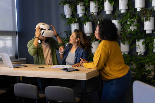 Diverse coworkers testing VR headset and using laptop on wooden table at office, copy space