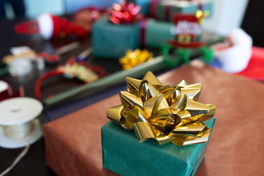 Small green gift box is sitting on brown wrapping paper on table, Christmas ribbons surrounding
