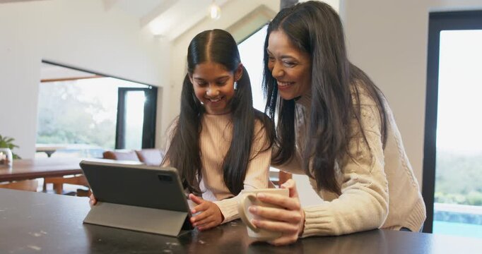 Placing hand on shoulder mother and daughter sharing high-five as navigating tablet at dining table