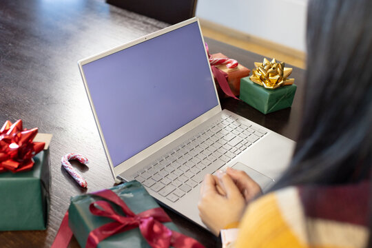 African American woman in striped sweater typing on laptop at home with wrapped Christmas gifts