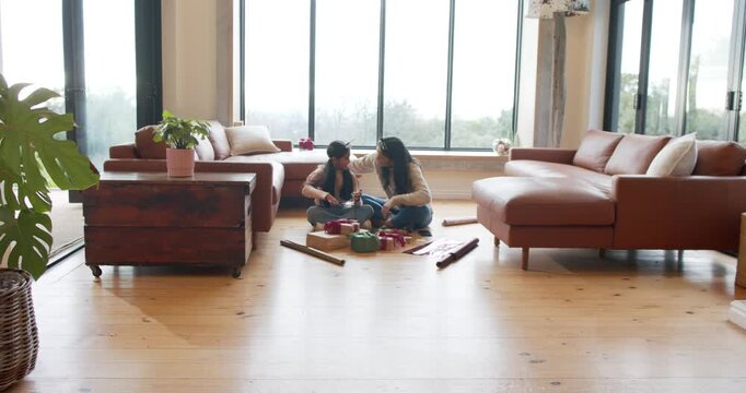 Amid paper and ribbons, diverse mother and daughter wrapping boxes, tying bows, hugging at home