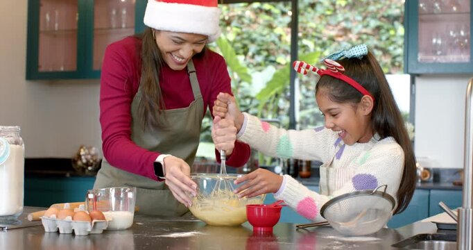 Diverse mother and daughter whisking batter in home kitchen after placing bowl for festive baking