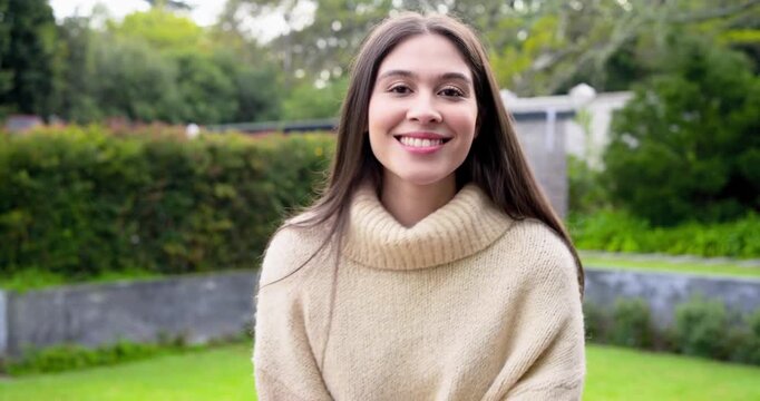 Female model facing camera adjusting hair by smartwatch, laughing in backyard engaging viewer