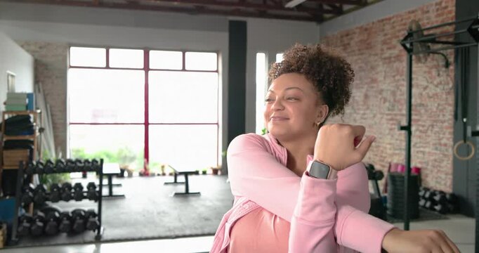 In gym woman warming up stretching shoulders swinging arms opening chest rolling neck near rings