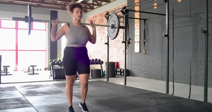 African American woman adjusting grip engaging core and performing barbell lunges at fitness studio