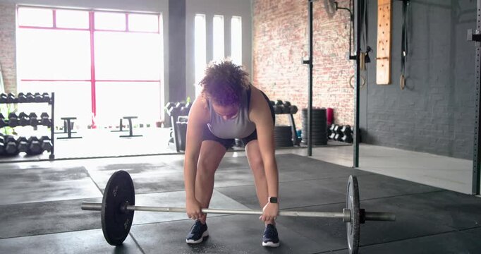 Rubbing hands, female athlete bending knees, pulling loaded barbell for workout at gym windows