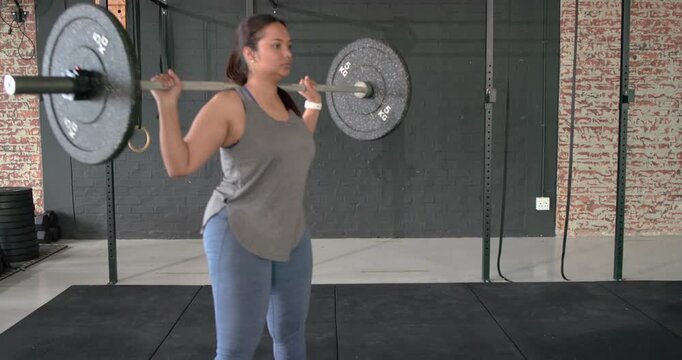 Asian woman athlete gripping barbell, stepping backward, squatting deeply for power at gym