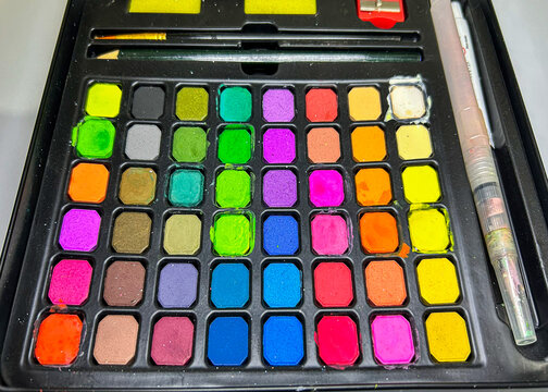 Complete vibrant neon watercolor paint set vector illustration, large makeup or face paint compact with multiple bright multi-colored square pans, brushes, and water brush pen on a black tray