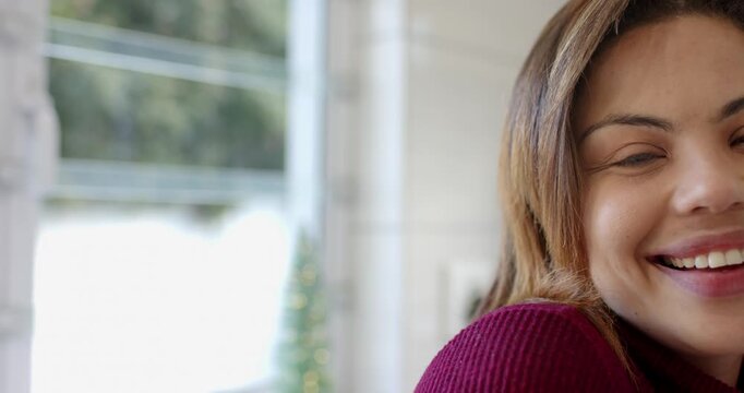 Camera filming woman smiling, blinking, and tilting head by home window near evergreen, copy space