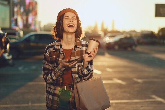 Smiling woman with coffee and shopping bag on urban street at golden hour, candid joyful portrait that highlights authenticity, mindful living and emotional storytelling in modern city life.