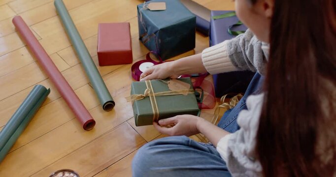 Adult female picking up green-wrapped box, tying twine into Christmas bow at home, copy space