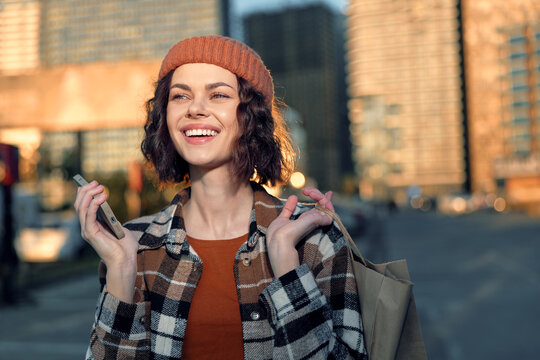 Woman smile in city street at golden hour, carrying shopping bag and wearing beanie and plaid jacket, candid lifestyle shot with authenticity, golden hour glow, mindful living.