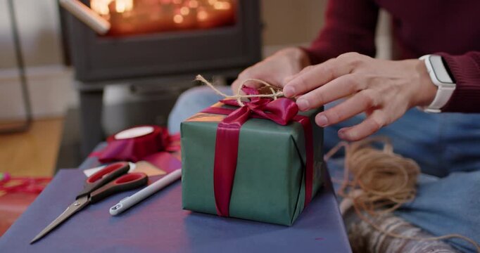 African American man in burgundy sweater preparing Christmas gift at home, tying twine on green box