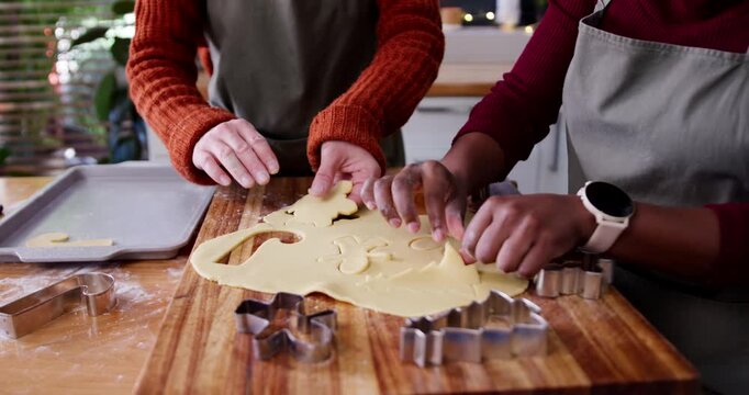 Diverse women rolling dough at wooden board pressing cutters and placing Christmas cookies on sheet
