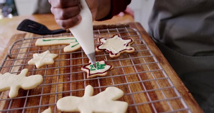 Woman guiding piping bag, adding green Christmas design on cookie at counter, hand entering frame