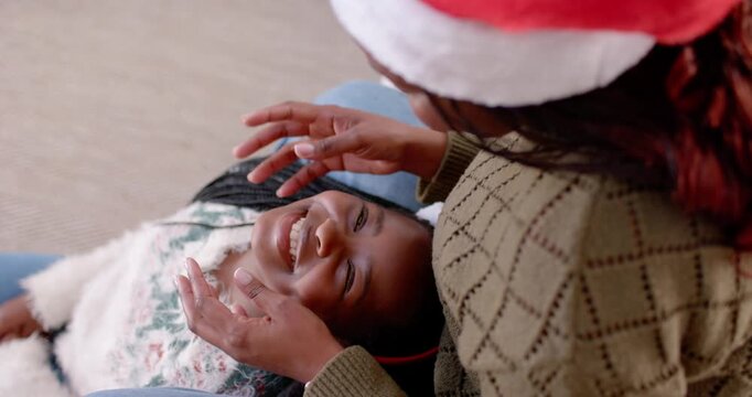 African mother leaning over, adjusting red headband and cupping child's face on couch at Christmas