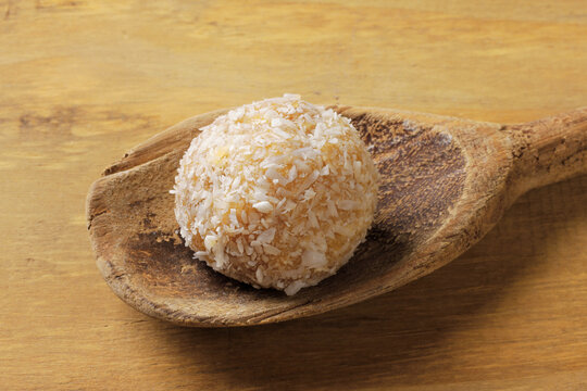 Brazilian coconut beijinho on a wooden spoon on a rustic wooden table. Traditional confectionery for parties and celebrations.