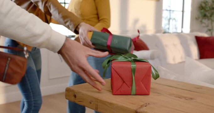 Diverse friends arriving, sparking hugs, placing red Christmas gift with green ribbon on wood table