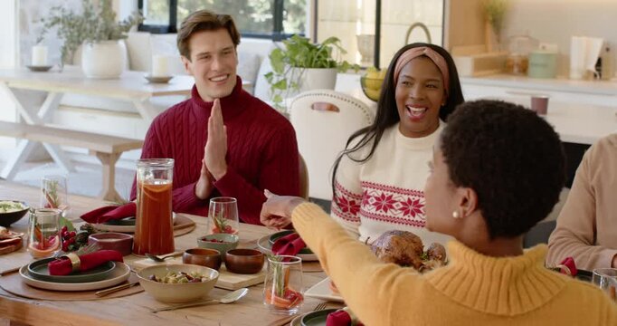 Friends sitting at dining table, woman presenting turkey causing man clapping and Christmas cheer