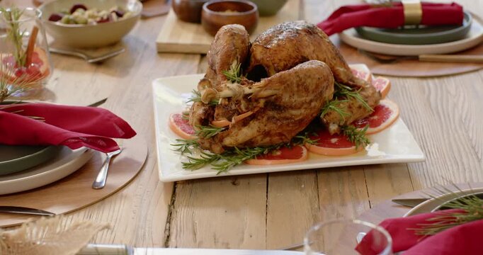 Camera is pulling back to show roasted turkey on platter on rustic dining table during Christmas