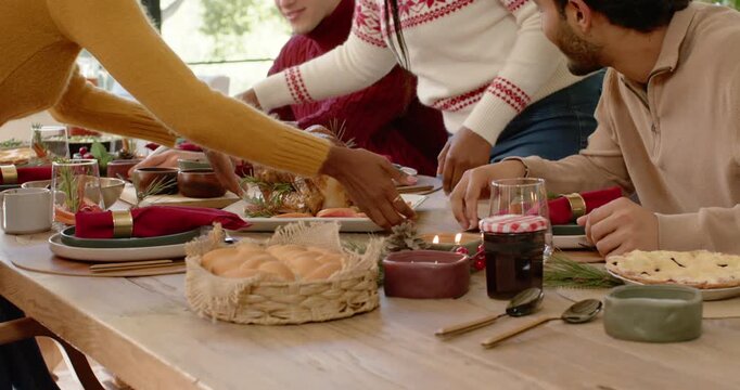 Diverse friends and family placing roasted turkey at wooden dining table, serving for Christmas