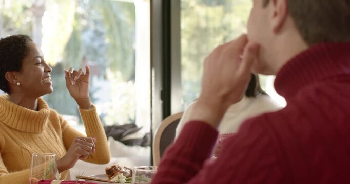 Diverse family at dining table, woman in mustard laughing at man telling Christmas story