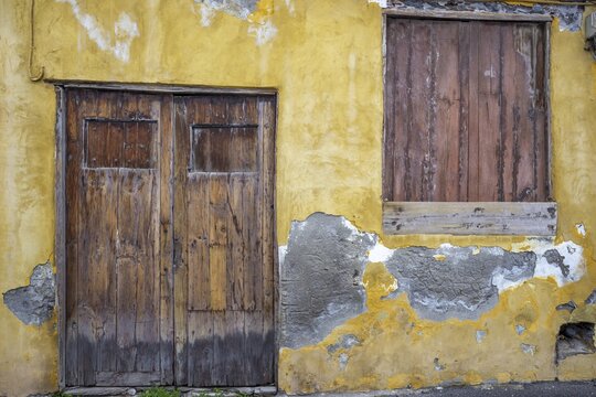 Weathered fa&ccedil;ade of an empty house in Garachico, characterized by crumbling plaster and old wooden doors, a silent testimony of past times, Garachico, Tenerife, Canary Islands, Spain