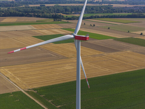 Aerial view of a wind turbine standing in a vast agricultural landscape with fields of varying colors and textures in Germany.