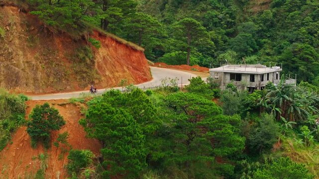 Motorcyclist rides a winding red hillside road in San Nicolas, Philippines