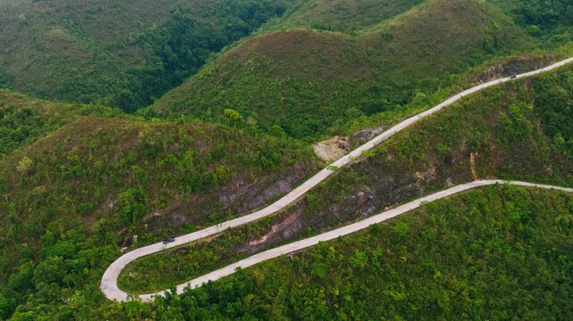 Dark car follows a sharp concrete switchback through green hills in Badian
