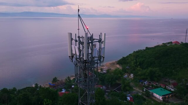 Drone orbits a coastal telecom tower under pink twilight skies in Alegria
