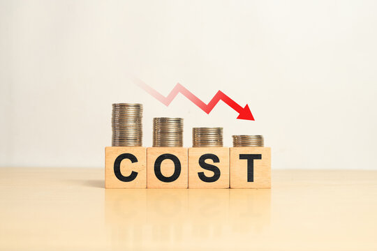Concept of cost reduction in business finance with wooden blocks spelling COST placed on descending stacks of coins, red downward arrow, symbolizing decreasing expenses, saving strategy, efficiency