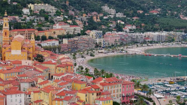 Colorful Menton buildings and church overlook a busy beach and marina on the coast