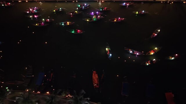 Colorful illuminated boats drift across dark water at night, showcasing a vibrant festival scene in Hoi An, Vietnam, with reflections and lights