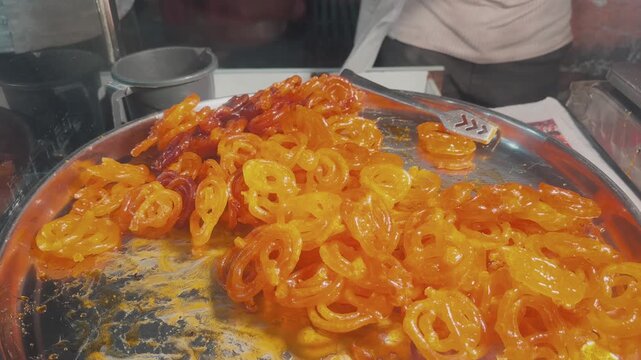 Close up shot of freshly prepared crispy jalebi piled on a large metal platter at a traditional Indian sweet stall
