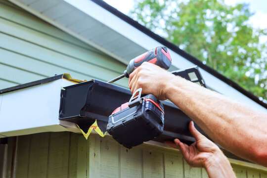 Worker uses drill to attach gutter to new house