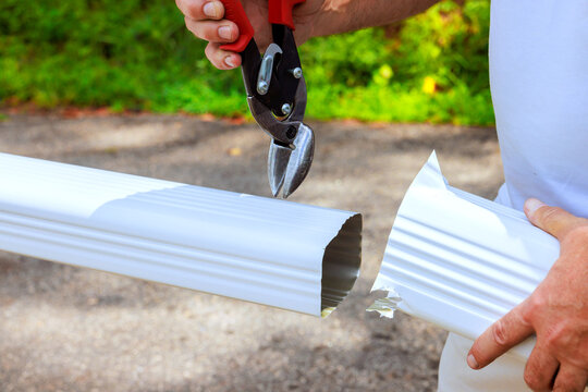 Contractor cuts white gutter pipe with pliers while standing on gravel path