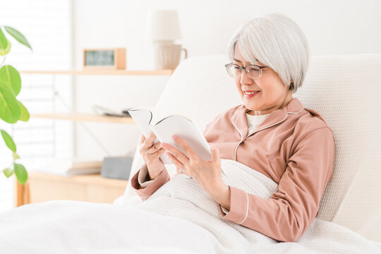 リクライニングベッドでくつろぎながら読書を楽しむシニア女性