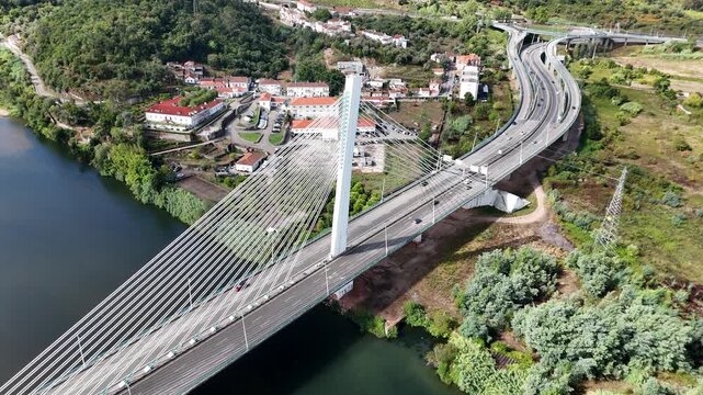 Aerial view of the cable-stayed Ponte Rainha Santa Isabel bridge spanning the Mondego River with traffic and surrounding green hills in Coimbra, Coimbra, Portugal.