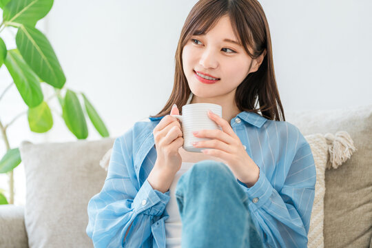 A woman relaxing on her sofa at home, sipping coffee and a hot drink.