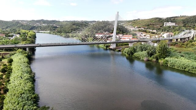 Aerial view of the cable-stayed Ponte Rainha Santa Isabel bridge spanning the Mondego River, surrounded by lush green riverbanks and rolling hills in Coimbra, Coimbra, Portugal.