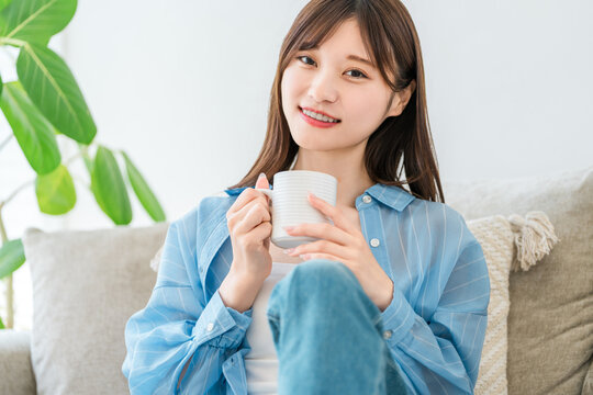 A woman relaxing on her sofa at home, sipping coffee and a hot drink.